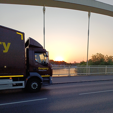 Gregory truck on bridge with sun setting.